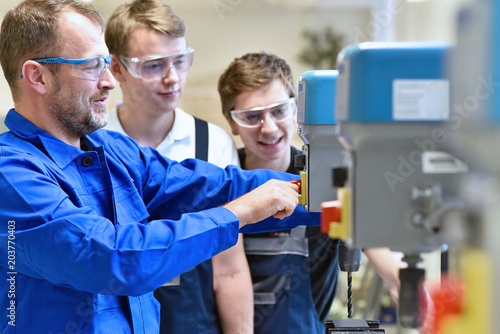 Group of young people in mechanical vocational training with teacher at drilling machine // Berufsausbildung - Jugendliche und Lehrer in der Berufsschule 