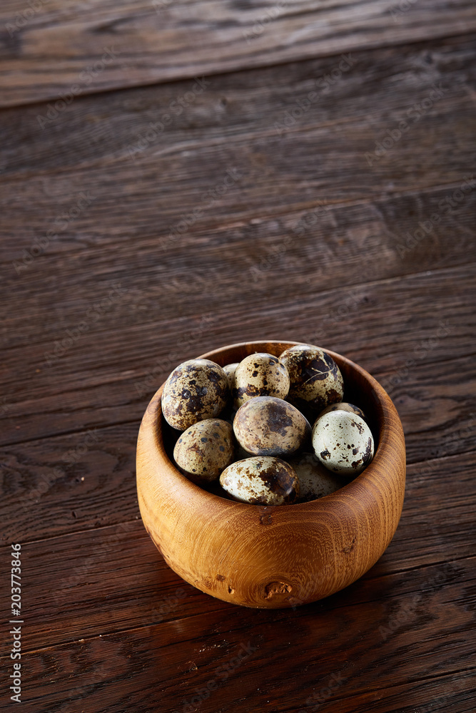 Fresh quail eggs in a wooden bowl on a dark wooden background, top view, close-up Fresh quail eggs in a wooden bowl on a dark wooden background, top view, close-up