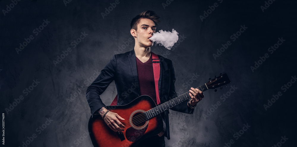 Handsome young musician with stylish hair in elegant clothes exhales smoke while playing acoustic guitar. Handsome young musician with stylish hair in elegant clothes exhales smoke while playing acoustic guitar.