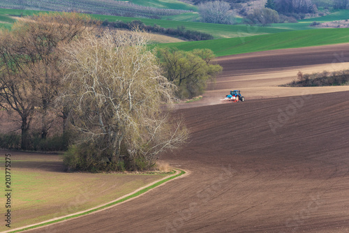 Obraz na płótnie Scenic View Of Farming BlueTractor With Red Harrow Which Plowing And Spraying Brown Spring Field. Small Blue Tractor Working On Brown Field. Tractor Cultivating Field. Agricultural Landscape. w salonie