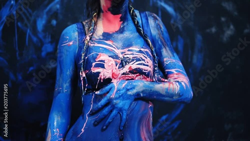 The sexy girl blurs the blue and pink paint erotically on her body, touches herself. Pink paint splash from the side. Slow motion