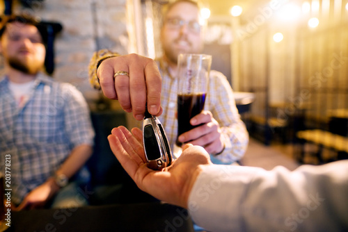 Drunk man with a beer in hand giving car key to the sober friend while enjoying in the bar. Close up focus view of key and hands. photo