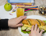 The girl collects a sandwich in school, on a table pencils, paper clips, apple, juice, dried fruits and textbooks