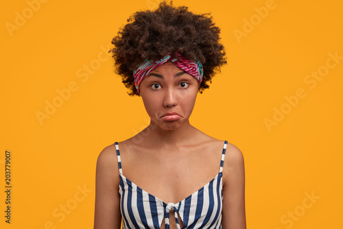 Pretty dark skinned female model looks in bewilderment  shocked to see something  wears casual sailor t shirt  isolated over yellow background. Lovely young African American housewife at home