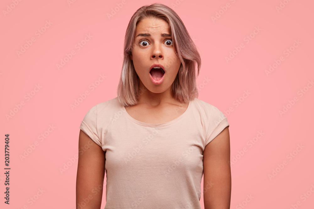 Image of frightened young European pretty female has wide opened mouth, stares at camera with bugged eyes, being scared by someone, expresses her big surprisement and astonishment, dressed casually. Image of frightened young European pretty female has wide opened mouth, stares at camera with bugged eyes, being scared by someone, expresses her big surprisement and astonishment, dressed casually.