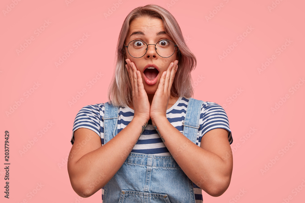 Attractive stylish teenager has shocked expression, looks with frustrated scared face, stares with eyes popped out, wears striped sailot t shirt and jean overalls, finds out bad surprising news Attractive stylish teenager has shocked expression, looks with frustrated scared face, stares with eyes popped out, wears striped sailot t shirt and jean overalls, finds out bad surprising news