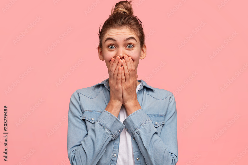 Young vivacious beautiful young female giggles joyfully, covers mouth, has fun alone, stands against pink background or studio wall, has natural laughter, hears positive story or funny anecdote Young vivacious beautiful young female giggles joyfully, covers mouth, has fun alone, stands against pink background or studio wall, has natural laughter, hears positive story or funny anecdote