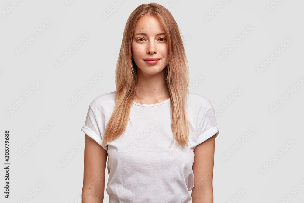 Portrait of pleased beautiful European female with long hair, dressed in casual t shirt, isolated on white background. Attractive woman student meets with groupmates. Facial expressions concept Portrait of pleased beautiful European female with long hair, dressed in casual t shirt, isolated on white background. Attractive woman student meets with groupmates. Facial expressions concept