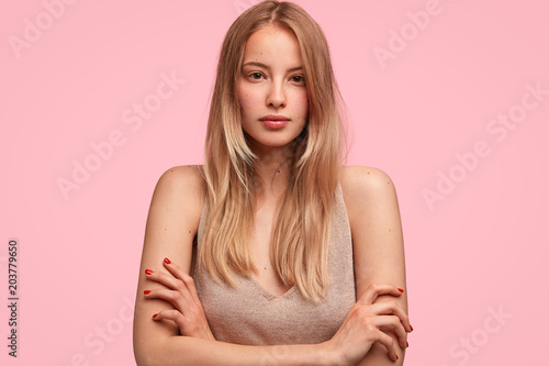 Horizontal portrait of attractive female keeps hands crossed, wears casual t shirt, poses at camera with serious expression, shows her natural beauty with no make up. People and lifestyle concept