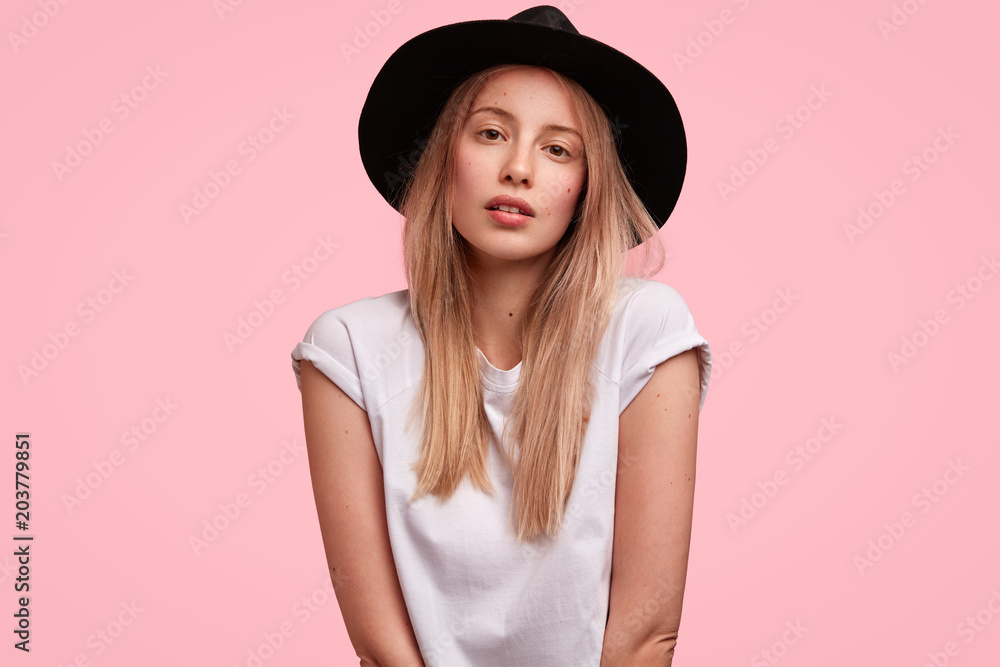 Beautiful fashion model in stylish summer hat, poses at camera with confident look, poses against pink studio background, likes to be photographed. Lovely young female spends leisure time alone Beautiful fashion model in stylish summer hat, poses at camera with confident look, poses against pink studio background, likes to be photographed. Lovely young female spends leisure time alone