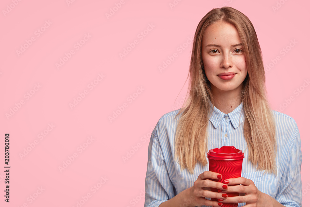 Lovely Caucasian female student has break after lectures, holds takeaway coffee, has pleasant talk with her groupmates, wears elegant shirt, poses against pink background with blank copy space Lovely Caucasian female student has break after lectures, holds takeaway coffee, has pleasant talk with her groupmates, wears elegant shirt, poses against pink background with blank copy space
