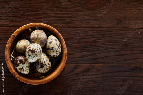 Fresh quail eggs in a wooden bowl on a dark wooden background, top view, close-up