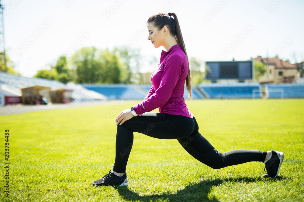 Young sport woman athlete stretches her leg on stadium green grass, healthy lifestyle concept