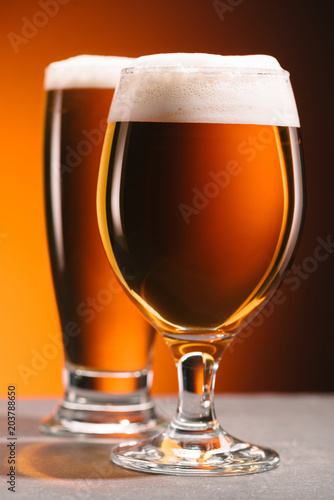 selective focus of arrangement of glasses of beer with froth on orange backdrop