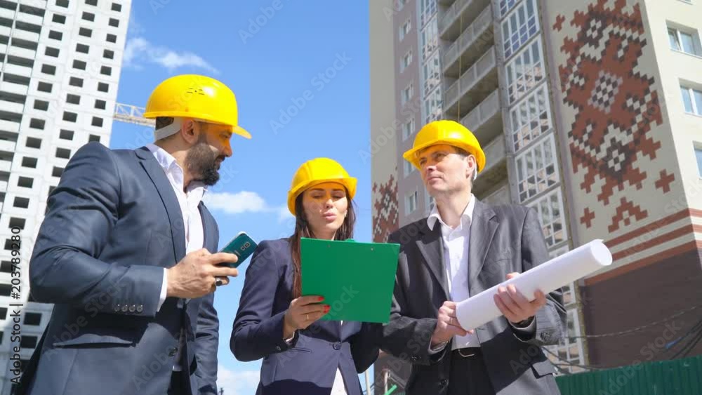 three businessmen an architect and an engineer stand on the construction site and study the blueprints of the project. the man is talking on the phone. the woman is looking at the tablet for papers three businessmen an architect and an engineer stand on the construction site and study the blueprints of the project. the man is talking on the phone. the woman is looking at the tablet for papers