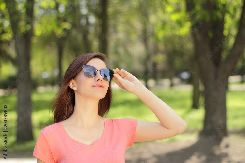 smiling young beautiful girl looking up, pretty woman in sunglasses and pink t-shirt, open air smiling young beautiful girl looking up, pretty woman in sunglasses and pink t-shirt, open air
