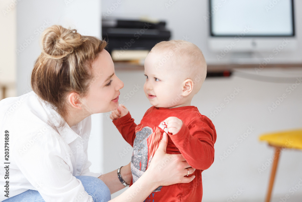 Smiling and joyful young mother plays with her baby boy two years old at home. Happy family spend time together. Motherhood and child Smiling and joyful young mother plays with her baby boy two years old at home. Happy family spend time together. Motherhood and child