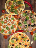 Four pizzas with different fillings on a wooden table. The view from the top.
