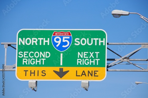 I-95 North South Second Right Next Right This Lane Green Yellow and Blue Sign Beneath Streetlight in a Sunny Late Afternoon with Blue Sky
