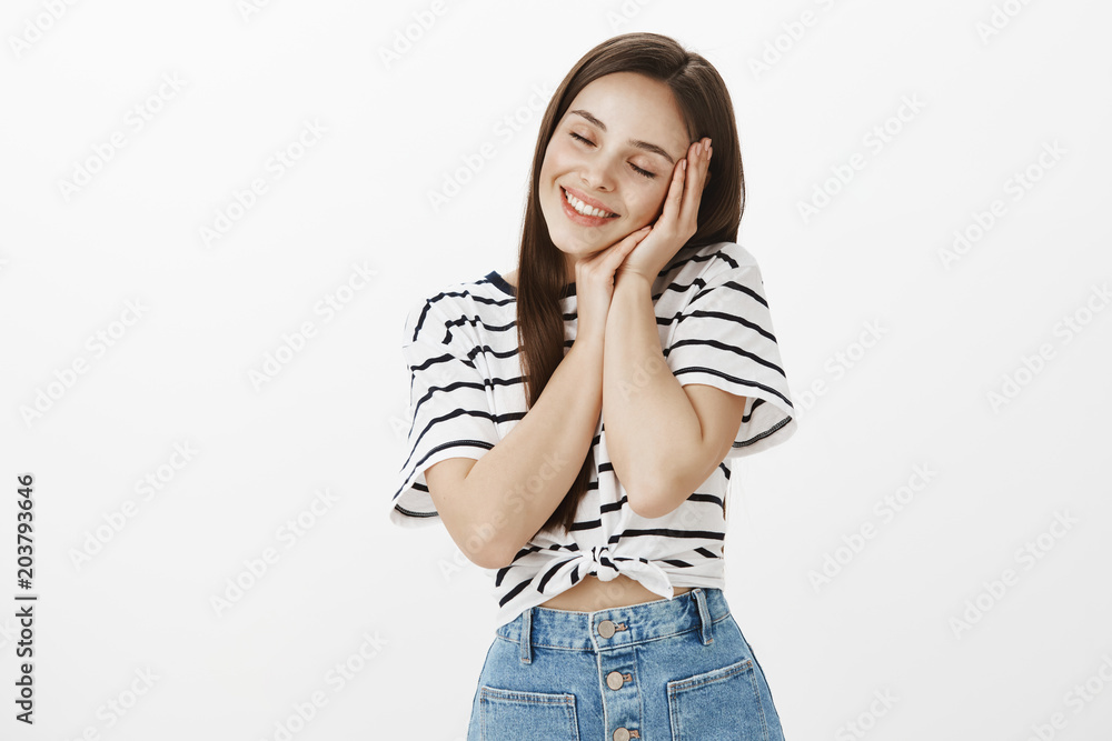 Feeling tender and beloved. Portrait of caring cute caucasian girlfriend in striped t-shirt, holding hands on cheek as if lying and sleeping, closing eyes and smiling sensually, being in dreamy mood Feeling tender and beloved. Portrait of caring cute caucasian girlfriend in striped t-shirt, holding hands on cheek as if lying and sleeping, closing eyes and smiling sensually, being in dreamy mood