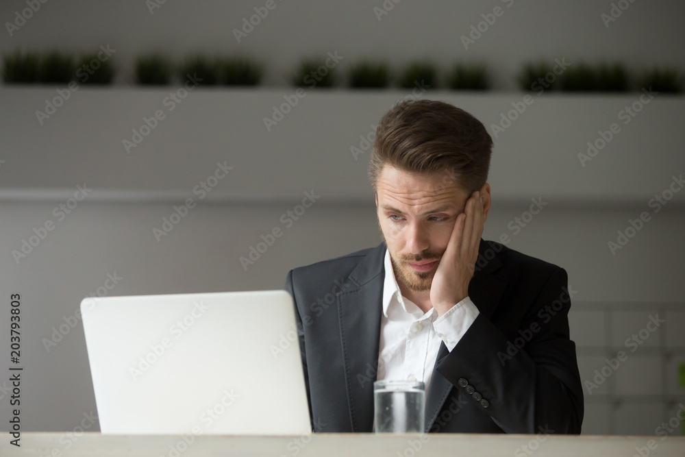 Frustrated and sad businessman hopelessly looking at laptop screen reading bad news of financial breakdown of his company. Concept of business collapse, bankruptcy and crisis Frustrated and sad businessman hopelessly looking at laptop screen reading bad news of financial breakdown of his company. Concept of business collapse, bankruptcy and crisis