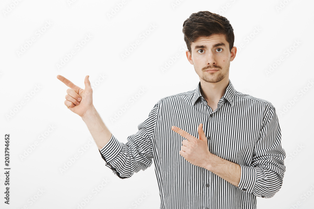 Shall we go. Portrait of confident serious young male coworker in striped shirt, pointing with finger gun gestures left, staring focused at camera, suggesting visit place in that direction Shall we go. Portrait of confident serious young male coworker in striped shirt, pointing with finger gun gestures left, staring focused at camera, suggesting visit place in that direction