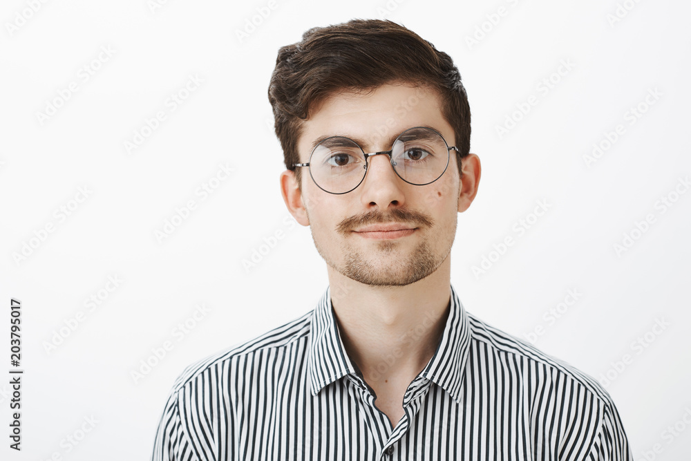 Portrait of friendly confident caucasian bearded guy with moustache, wearing glasses, smiling politely and looking relaxed and calm over gray background, listening to customer complaint over gray wall Portrait of friendly confident caucasian bearded guy with moustache, wearing glasses, smiling politely and looking relaxed and calm over gray background, listening to customer complaint over gray wall