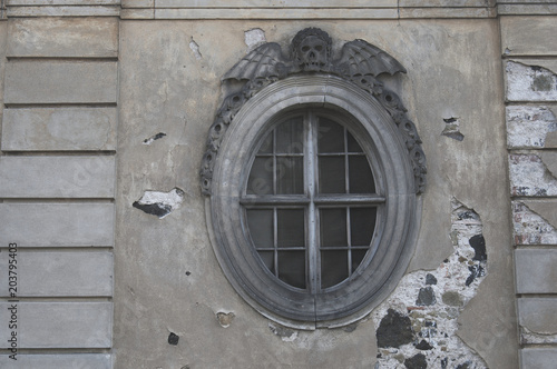 Round window of the church morgue with skull and wings on the top. Horizontal shot with damaged plaster.