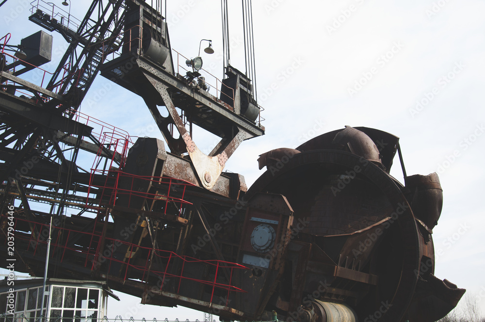 Fototapeta premium The huge coal mining machine captured with focus on mining wheel and structure in the front part of the machine.
