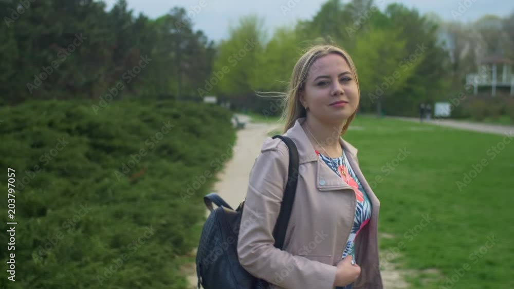 Lovely teenage girl with straight long blonde hair turning back and smiling while walking on footpath in parkland. Rear view. Playful young woman with flying hair in the wind looking back and smiling. Lovely teenage girl with straight long blonde hair turning back and smiling while walking on footpath in parkland. Rear view. Playful young woman with flying hair in the wind looking back and smiling.