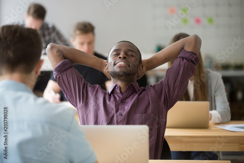 Satisfied black worker leaning back in chair with eyes closed in coworking space. Happy african american relaxing hearing good news on company business success on stock exchange. Concept of rewarding © fizkes
