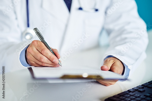 Foto Male doctor writes notes on the clipboard in medical clinic
