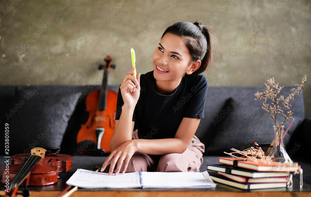 The beauty is sitting on sofa beside violin,raise pen up in the air with  smile and happy face,thinking about work,home office studio,blurry light  around. Stock Photo
