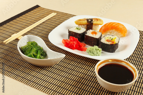 Sushi with omelet with eel and with salmon, rolls, hiyashi wakame salad and soy sauce on a bamboo mat close up.