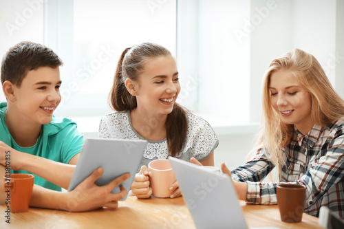 Group of cool teenagers with modern devices resting in cafe