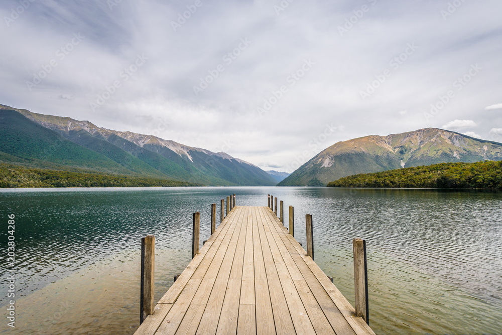 Lake Rotoiti, Tasman, Nelson Lakes, New Zealand: Beautiful scenic view to great mountain range lake with wooden jetty pier and pretty smooth reflections on the water surface at a cloudy rainy day