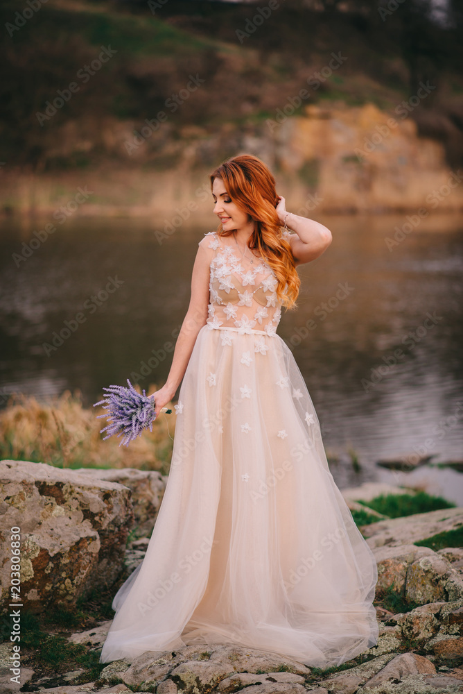 young red-haired woman standing with flowers in hands and smiling against the background of the river young red-haired woman standing with flowers in hands and smiling against the background of the river