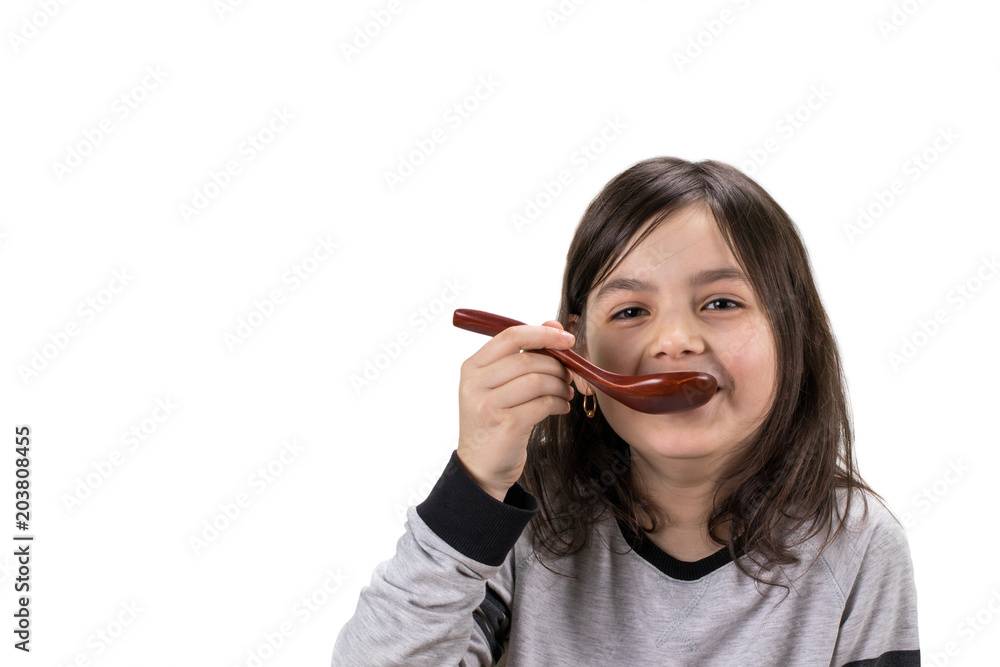 Portrait of girl with wooden spoon in her mouth, isolated on white background with copy space Portrait of girl with wooden spoon in her mouth, isolated on white background with copy space