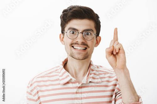 Portrait of intense serious european male teacher in round glasses  raising index finger in eureka or while tutoring  explaning homework  being overwhelmed and excited with loving work over gray wall