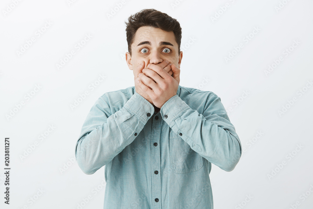 Portrait of shocked scared young guy in casual clothes, covering mouth with palms and staring with popped eyes at camera, wanting scream from fear, feeling terrified over gray background Portrait of shocked scared young guy in casual clothes, covering mouth with palms and staring with popped eyes at camera, wanting scream from fear, feeling terrified over gray background