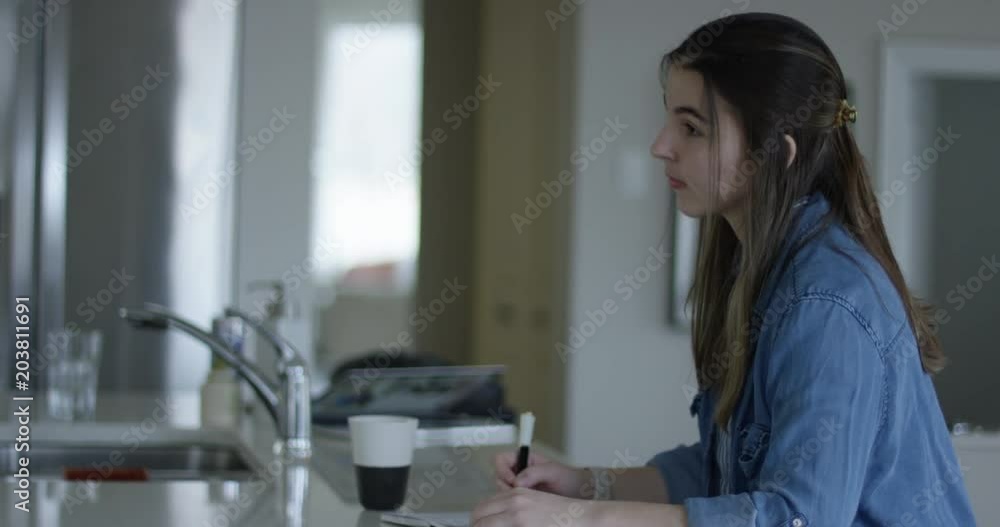 Young woman writing notes on kitchen counter Young woman writing notes on kitchen counter