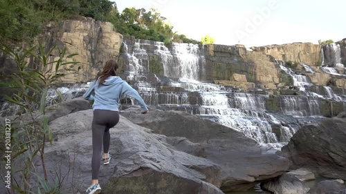 Woman climbing on rock, raising hands, standing near Pongour waterfall in Dalat