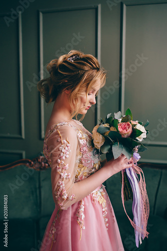 portrait of a young woman in a pink dress holding a bouquet in her hands against a vintage interior background