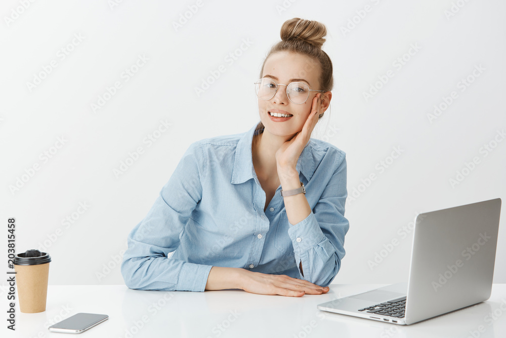 Casual working day in office. Portrait of positive good-looking businesswoman in glasses, sitting near laptop smartphone and drinking coffee, gazing at camera while having break during worktime Casual working day in office. Portrait of positive good-looking businesswoman in glasses, sitting near laptop smartphone and drinking coffee, gazing at camera while having break during worktime