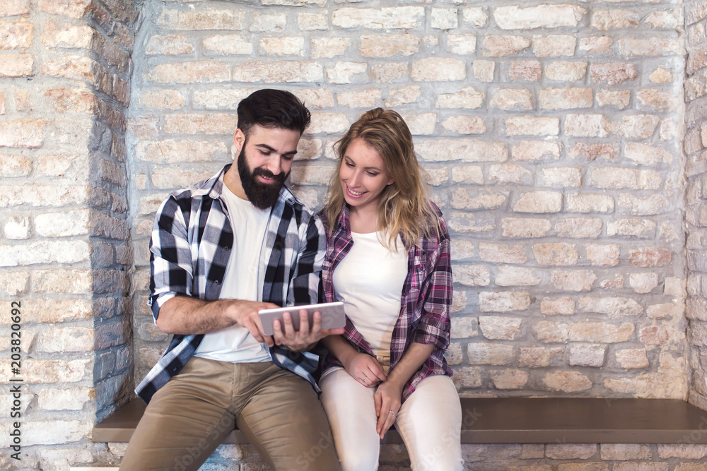 Happy young couple using digital tablet on a brick wall background Happy young couple using digital tablet on a brick wall background
