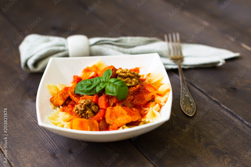 Italian pasta - butterfly macaroni (bows) of Farfarello with tomato sauce on a white plate and on a dark wooden background. Italian pasta - butterfly macaroni (bows) of Farfarello with tomato sauce on a white plate and on a dark wooden background.