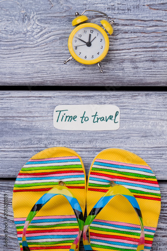 Summer sandals and clock, flat lay. Time to travel to resort vacation, dark wooden surface background. photo