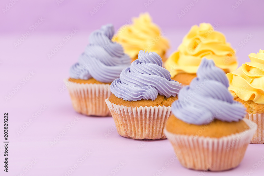 Cupcakes decorated with yellow and violet cream decorations on pastel background.