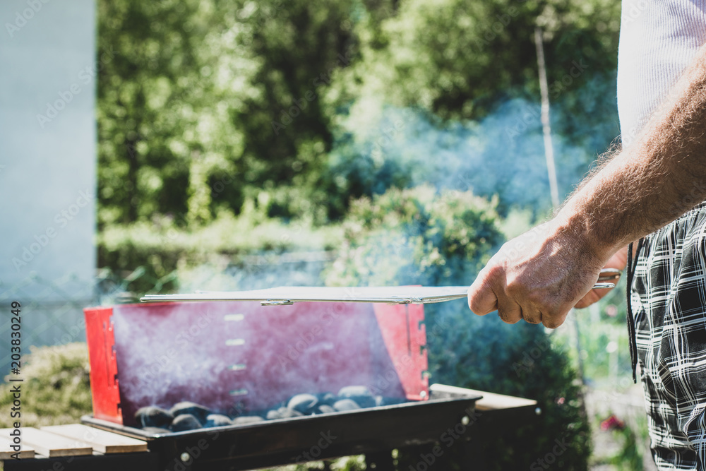 Burning barbecue. The man fires up the grill. The man puts the grate on the grill. Spending time together with the family at the grill. Social meetings, friends. Red gril with kindling and coal. Burning barbecue. The man fires up the grill. The man puts the grate on the grill. Spending time together with the family at the grill. Social meetings, friends. Red gril with kindling and coal.