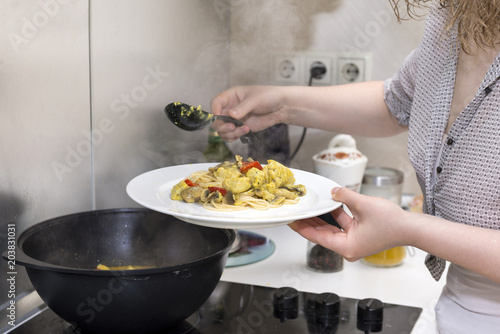 girl puts in a plate of cooked pasta with chicken fillet, mushrooms and pepper in a creamy sauce